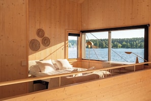 A cabin with a bed, a window, and a view of a lake. - Stay North - Loviisa Floating House (Loviisa)