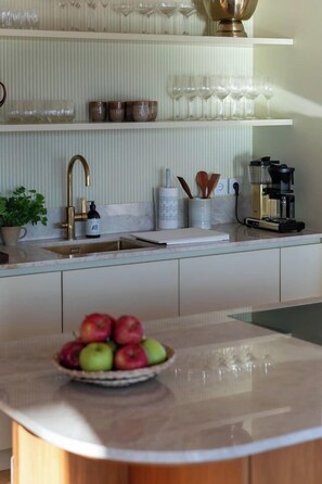 A kitchen with a marble countertop, a bowl of fruit, a coffee maker, and a shelf with glassware. - Stay North - Loviisa Floating House (Loviisa)