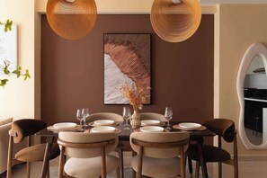 A dining area with a table set for four, surrounded by chairs, a vase with dried flowers, and a large abstract painting on the wall. - 3BR/4Beds | 2BA • Central D1 • Group Stay • Corner (Thành phố Hồ Chí Minh)