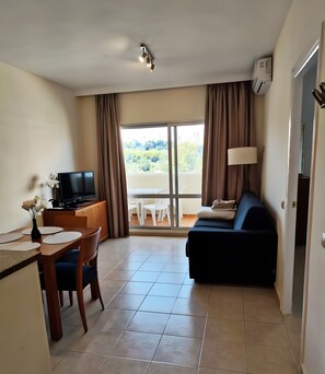A hotel room with a dining area, a sofa, a TV, and a balcony with curtains. - 1-Bedroom Apartment in Benalbeach with Pool, Private Terrace & Air Conditioning (Benalmádena)