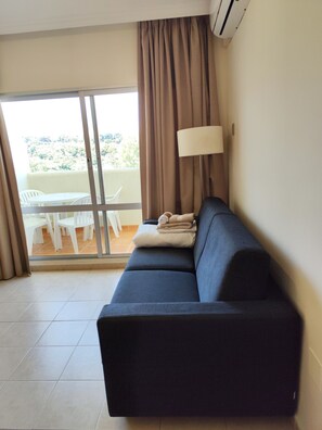 A room with a sofa, a lamp, a table with chairs, and a view through a glass door. - 1-Bedroom Apartment in Benalbeach with Pool, Private Terrace & Air Conditioning (Benalmádena)
