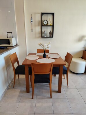 A dining area with a table set for four, surrounded by chairs, a vase with flowers, and a wall-mounted clock. - 1-Bedroom Apartment in Benalbeach with Pool, Private Terrace & Air Conditioning (Benalmádena)