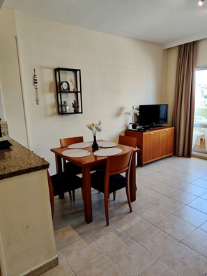 A dining area with a table, chairs, and a television in the background. - 1-Bedroom Apartment in Benalbeach with Pool, Private Terrace & Air Conditioning (Benalmádena)