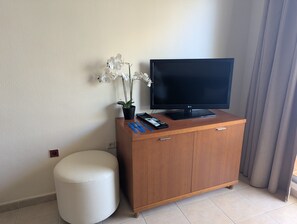 Ein Hotelzimmer mit Holzschrank, Flachbildfernseher, Topf-Orchidee, Fernbedienung und weißem Hocker.