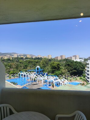 Blick auf einen Poolkomplex mit mehreren Wasserrutschen und einer umliegenden Grünanlage mit Gebäuden im Hintergrund.