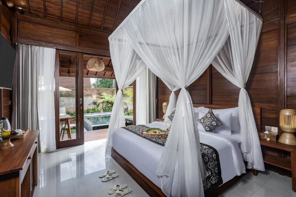 A four-poster canopy bed with a view of a pool and garden.