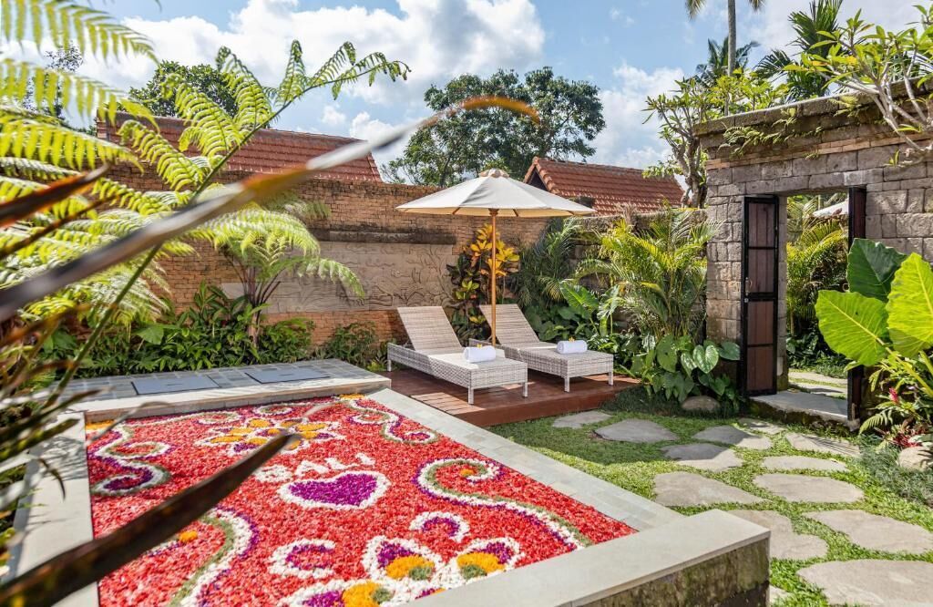 Un jardín con un parterre floral, dos sillones de descanso y un muro de piedra.