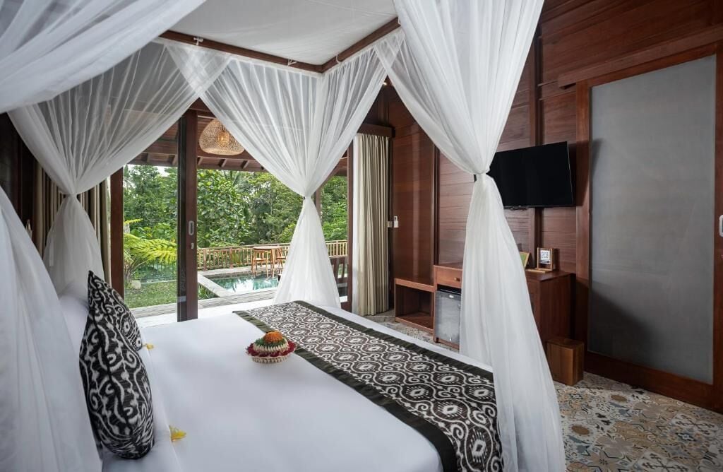 A bedroom with a bed, a television, and a view of the outdoors.