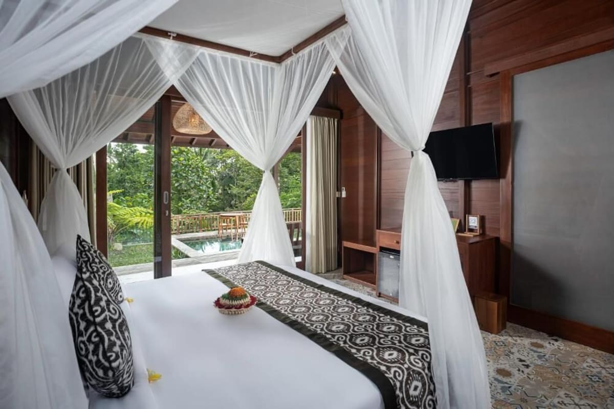 A bedroom with a bed, a television, and a view of the outdoors.