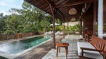 A poolside area with a wooden deck, lounge chairs, and a covered seating area.