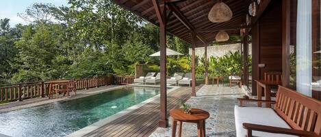 A poolside area with a wooden deck, lounge chairs, and a covered seating area.