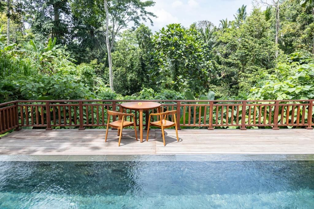 Una terraza de madera con piscina, rodeada de exuberante vegetación.