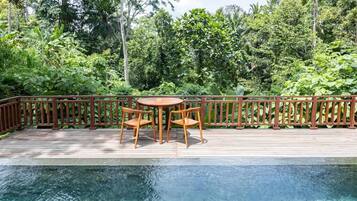 Una terraza de madera con piscina, rodeada de exuberante vegetación.