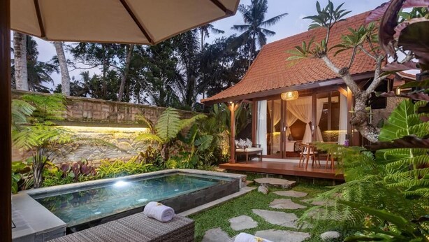 Un área de piscina privada con sillas de descanso, un muro de piedra y plantas tropicales.