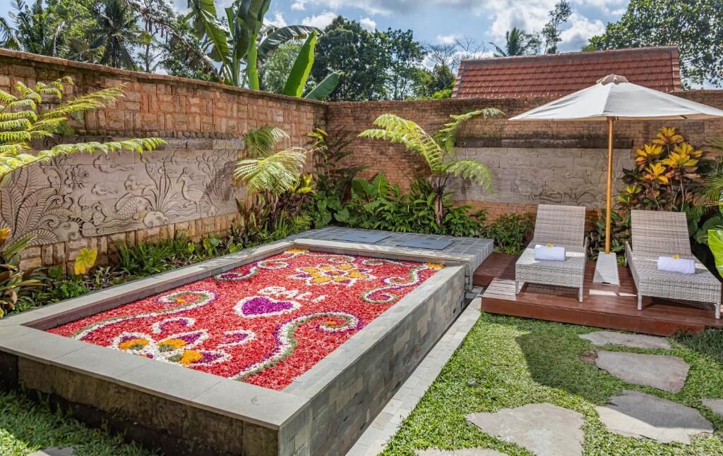 A garden with a patterned flower bed, a brick wall with carvings, and a seating area with a canopy.