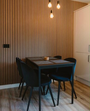 A dining area with a wooden slat wall, a round table, and four chairs. - The Milburn-sleeps6-enclosedgarden-nearglasgow (Renfrew)