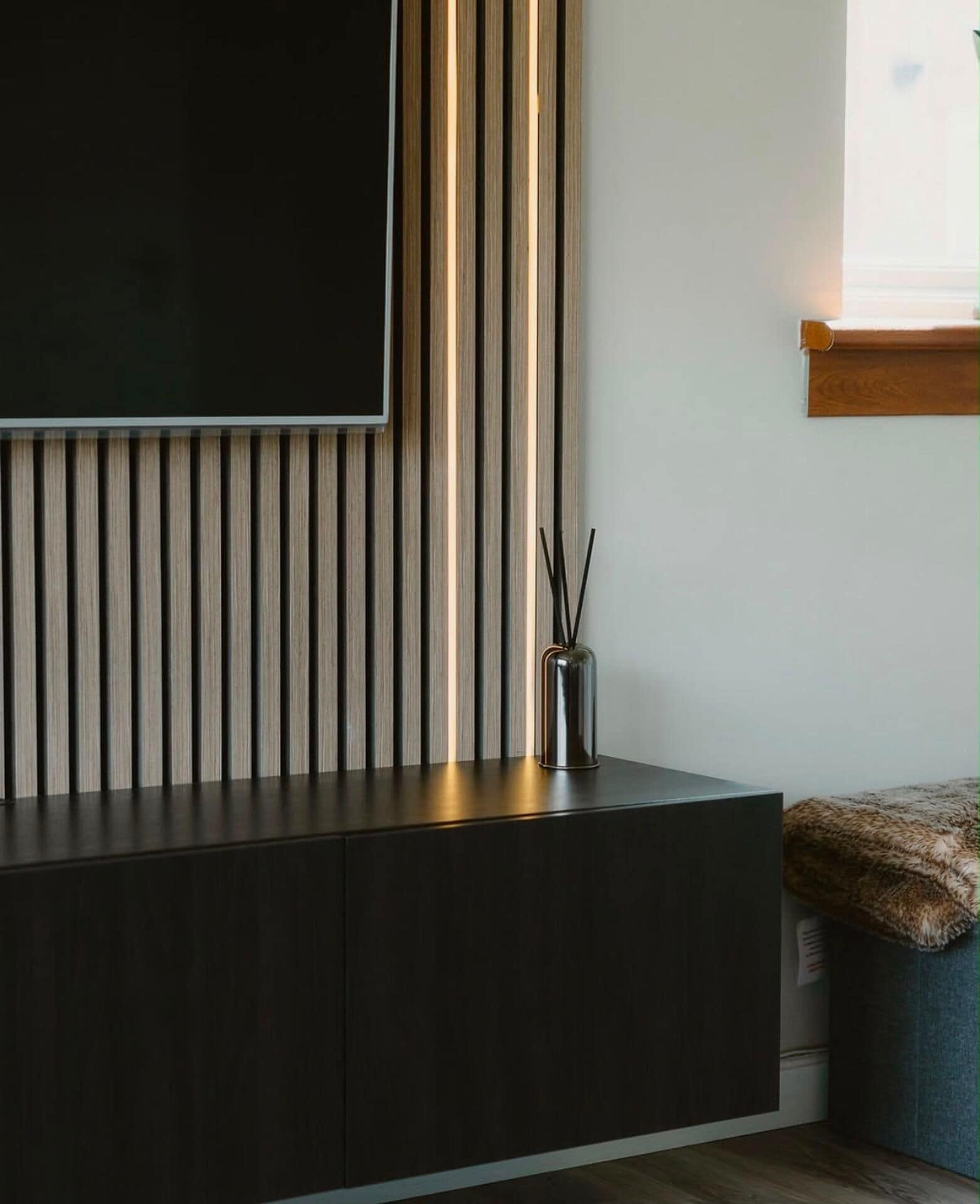 A modern living space with a dark-colored entertainment unit, a wall-mounted TV, and a vertical light strip.