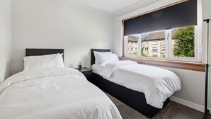 Hotellihuone, jossa on kaksi sänkyä, ikkuna, josta on näkymä rakennuksiin, ja kattovalaisin.