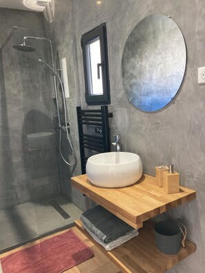 Une salle de bain moderne avec une douche à parois de verre, un miroir rond et un meuble-lavabo en bois avec un vasque blanche.