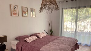 A bedroom with a bed, a bedside table, a lamp, and a window with a view of trees. - Room with bathroom, toilet, and terrace, 200 meters from the Saumane Golf Course (Saumane-de-Vaucluse)