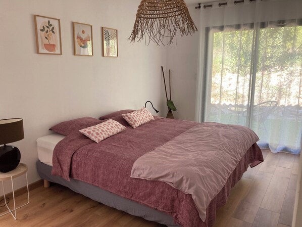 Une chambre à coucher avec un lit, une table de chevet, une lampe et une fenêtre donnant sur des arbres.