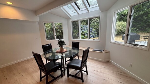 A dining area with a glass table and chairs, large windows with views of greenery, and a skylight. - Spacious 4-bedroom house in beautiful Bellevue with AC (Bellevue)