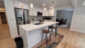 A modern kitchen with white cabinetry, stainless steel appliances, and a central island with bar stools. - Spacious 4-bedroom house in beautiful Bellevue with AC (Bellevue)