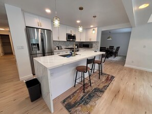 A modern kitchen with white cabinetry, stainless steel appliances, and a central island with bar stools. - Spacious 4-bedroom house in beautiful Bellevue with AC (Bellevue)