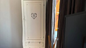 A room with a white cabinet featuring a decorative heart emblem, a wooden floor, and a table with a bottle and a black object. - La Rocca Guest House & SPA - Standard Room 5 (Montefalco)