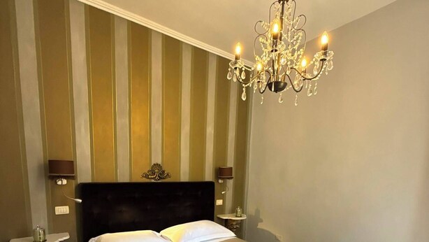 A hotel room with a large bed, a chandelier, and striped wallpaper. - La Rocca Guest House & SPA - Standard Room 5 (Montefalco)