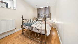 A bedroom with a metal bed frame, a white radiator, wooden flooring, and a window with a curtain. - Comfy Bishopsworth Apartment for Work & Long Stays (Bishopsworth)
