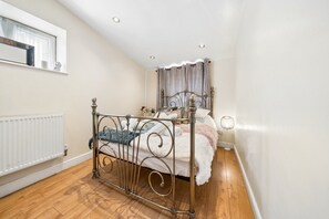 Ein Schlafzimmer mit einem Metallbettgestell, einem weißen Heizkörper, Holzböden und einem Fenster mit Vorhang.