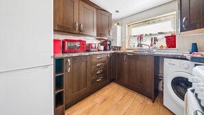 A compact kitchen with wooden cabinets, a microwave, a toaster, and a washing machine. - Comfy Bishopsworth Apartment for Work & Long Stays (Bishopsworth)