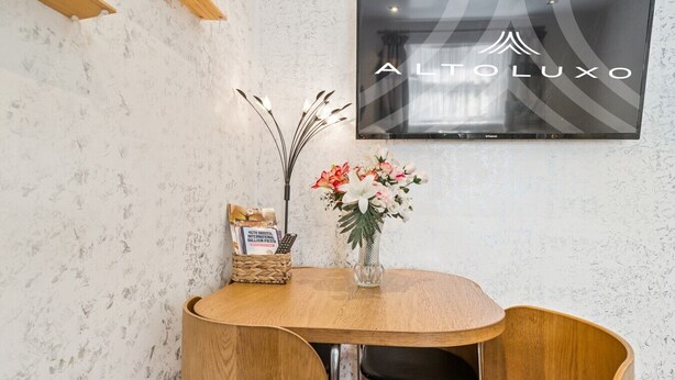A small wooden table with a vase of flowers, a basket with a balloon-themed item, and a wall-mounted television. - Comfy Bishopsworth Apartment for Work & Long Stays (Bishopsworth)