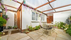 A greenhouse with a wooden table and chairs, surrounded by potted plants and flowers. - Comfy Bishopsworth Apartment for Work & Long Stays (Bishopsworth)