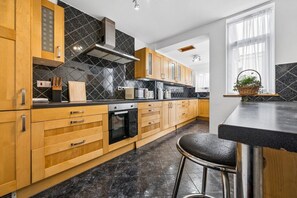 Eine moderne Küche mit Holzschränken, einer schwarzen Fliesenrückwand, Edelstahlgeräten und einem Barhocker.