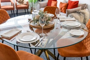 A round glass table set for dining with plates, cutlery, and glasses, surrounded by orange upholstered chairs. - HardenhuishHaus|Spacious 4BR|Group Stay|Parking (Brislington)