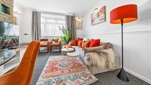 Una sala de estar moderna con un sofá, sillas, una mesa de centro, un televisor y una lámpara de pie.