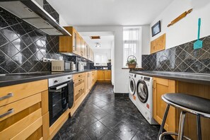 Eine moderne Küche mit schwarz-weißen Fliesen, Holzschränken, einem Einbauofen, einer Waschmaschine und einem Barhocker.