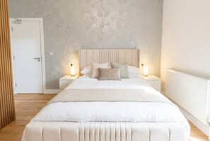 A bedroom with a large bed, two bedside tables, and a wall with a leaf pattern. - 2|Burnham-on-sea|Contractors|Couple|Sleeps2|WiFi (Somerset)