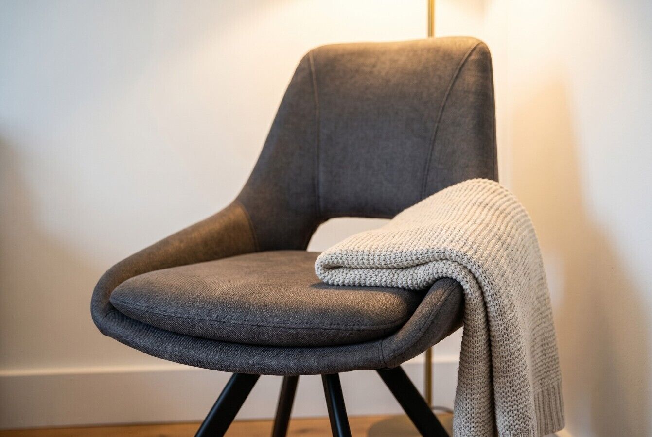 A chair with a grey upholstered seat and black metal legs, positioned against a plain wall.