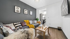 Ein modernes Wohnzimmer mit grauem Sofa, einem Holztisch und gerahmten Kunstwerken an der Wand.