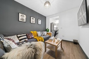 A modern living room with a grey sofa, a wooden coffee table, and framed artwork on the wall. - Inviting Deluxe Home: Ideal for Group|Family Stays (Brislington)