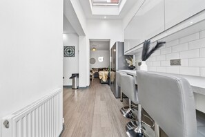 A modern kitchen with a skylight, white tiled backsplash, and a central island with bar stools. - Inviting Deluxe Home: Ideal for Group|Family Stays (Brislington)