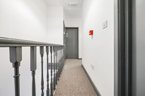 A narrow hallway with a carpeted floor, a metal railing, and a door at the end. - Inviting Deluxe Home: Ideal for Group|Family Stays (Brislington)