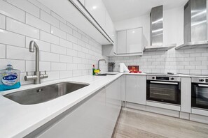 A modern kitchen with white cabinetry, stainless steel appliances, and a built-in oven. - Inviting Deluxe Home: Ideal for Group|Family Stays (Brislington)