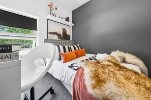 A bedroom with a bed, a desk, and a chair. There is a window with a view of trees. - Inviting Deluxe Home: Ideal for Group|Family Stays (Brislington)