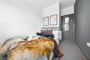 A bedroom with a bed, pillows, a blanket, and a fur rug. There is a door and a radiator on the wall. - Inviting Deluxe Home: Ideal for Group|Family Stays (Brislington)