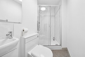 Un baño moderno con ducha envuelta en vidrio, un lavamanos blanco y un inodoro.