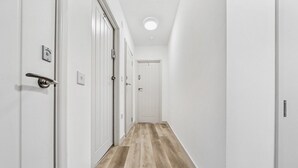Kapea käytävä, jonka seinät ovat valkoiset ja lattia puuta, johtaa käytävän päässä olevaan oveen.